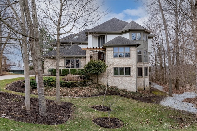 rear view of property featuring brick siding, a lawn, and a shingled roof