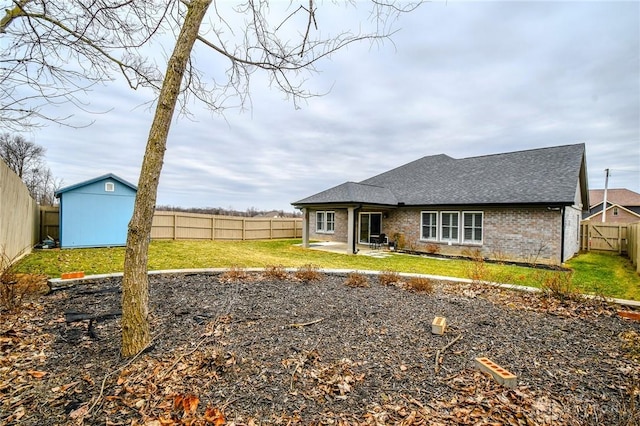 back of property featuring roof with shingles, brick siding, a patio, a fenced backyard, and an outdoor structure