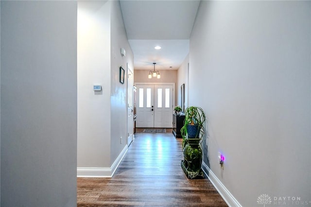 corridor featuring a notable chandelier, baseboards, and wood finished floors