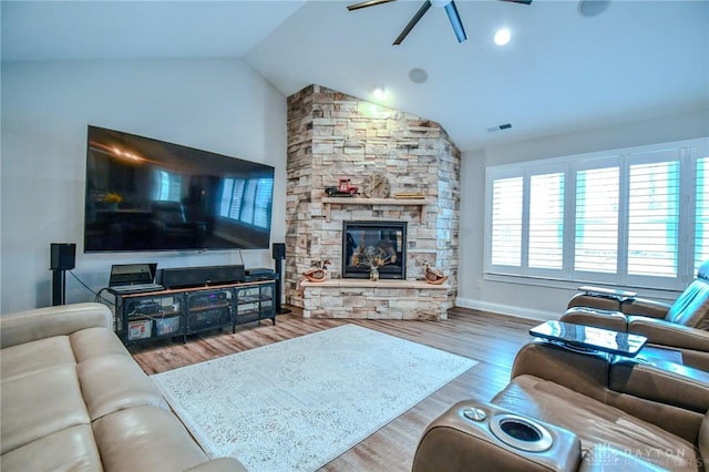 living area with visible vents, vaulted ceiling, a stone fireplace, and wood finished floors