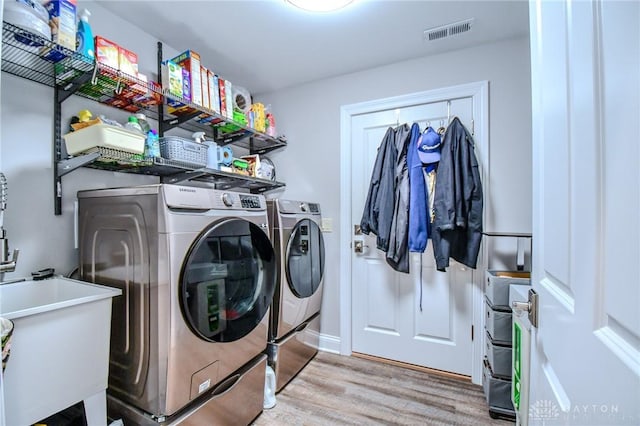 clothes washing area featuring laundry area, visible vents, light wood-style flooring, washer and dryer, and a sink