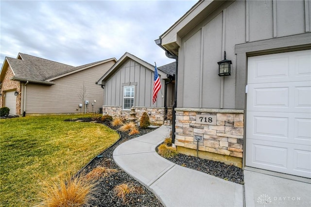 view of exterior entry with a garage, stone siding, board and batten siding, and a lawn