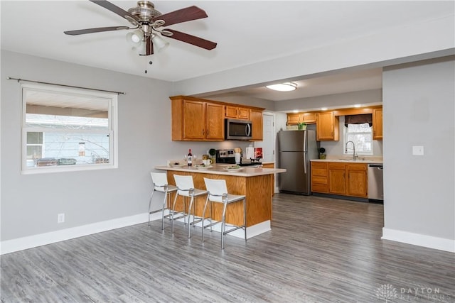 kitchen with stainless steel appliances, a peninsula, a sink, baseboards, and light countertops