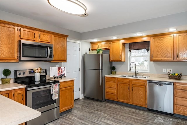 kitchen with appliances with stainless steel finishes, light countertops, a sink, and dark wood-style floors