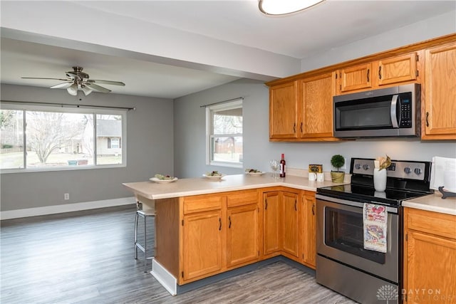 kitchen featuring baseboards, appliances with stainless steel finishes, a peninsula, light countertops, and light wood-type flooring