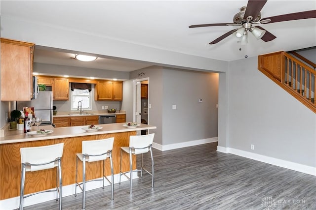 kitchen with light countertops, appliances with stainless steel finishes, a sink, a peninsula, and baseboards