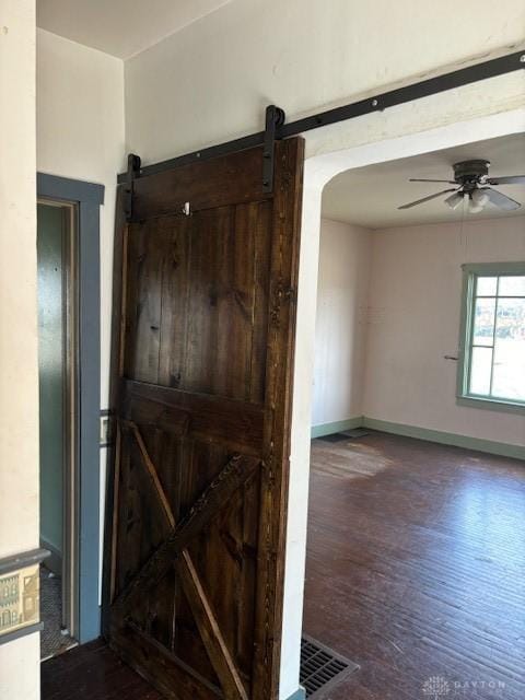 spare room featuring a barn door, visible vents, baseboards, ceiling fan, and wood finished floors