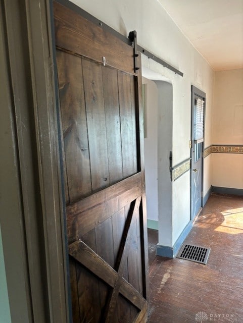 hallway featuring dark wood-style floors, a barn door, visible vents, and baseboards