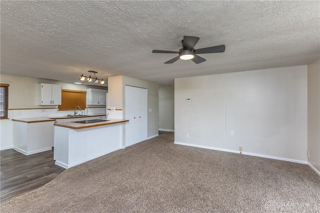 kitchen featuring a textured ceiling, a sink, baseboards, white cabinets, and dark colored carpet