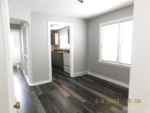 interior space featuring arched walkways, a sink, dark wood finished floors, and baseboards