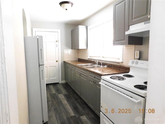 kitchen featuring gray cabinetry, under cabinet range hood, white appliances, a sink, and backsplash