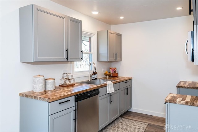 kitchen featuring gray cabinetry, dark wood finished floors, butcher block countertops, appliances with stainless steel finishes, and a sink