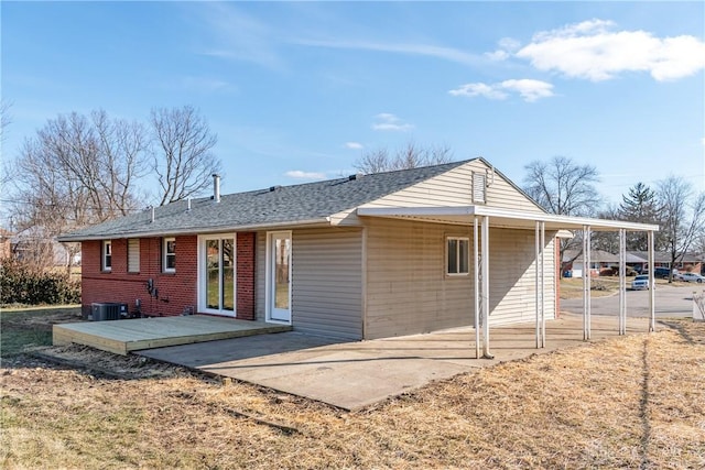 rear view of house with brick siding, a shingled roof, a carport, cooling unit, and a patio area