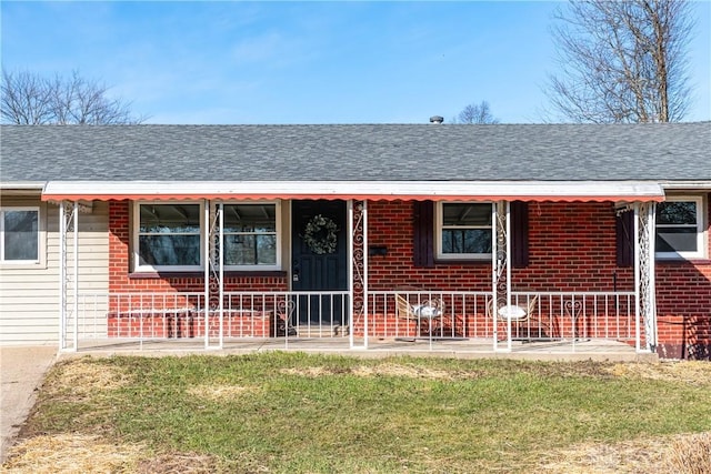 view of front of property with brick siding, covered porch, a front lawn, and roof with shingles
