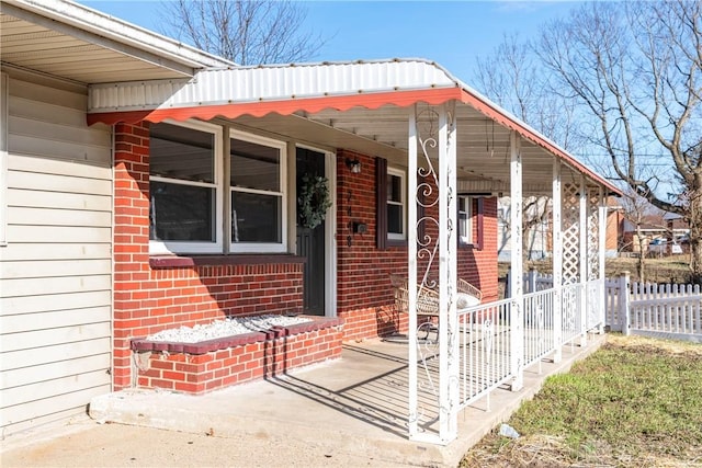 view of exterior entry with covered porch, fence, and brick siding