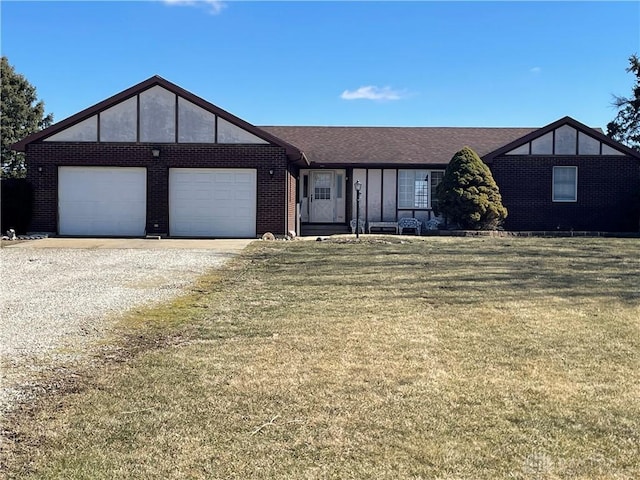 english style home featuring an attached garage, brick siding, a shingled roof, a front lawn, and gravel driveway