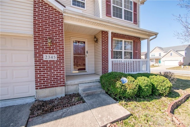 doorway to property featuring a garage, brick siding, and a porch