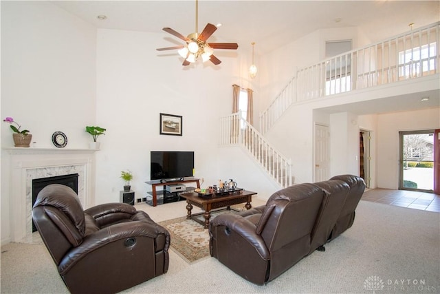 living room with a ceiling fan, stairway, a high ceiling, carpet floors, and a fireplace