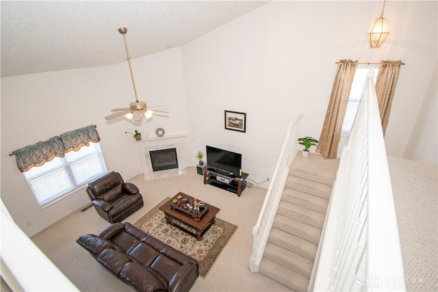 carpeted living area with high vaulted ceiling, a premium fireplace, stairway, and a ceiling fan