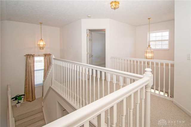 hall featuring carpet, a textured ceiling, an upstairs landing, and an inviting chandelier