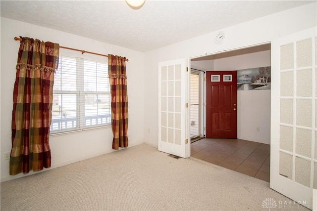 tiled spare room featuring a textured ceiling, french doors, and carpet