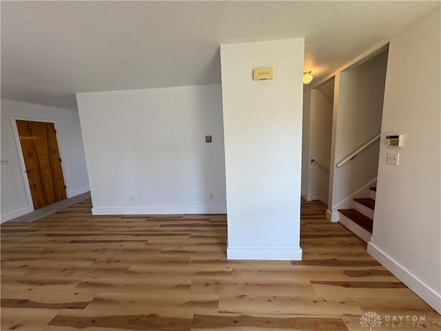 spare room featuring baseboards, stairway, and light wood finished floors