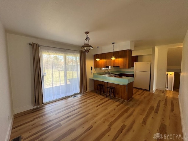 kitchen featuring light wood finished floors, light countertops, visible vents, freestanding refrigerator, and a peninsula