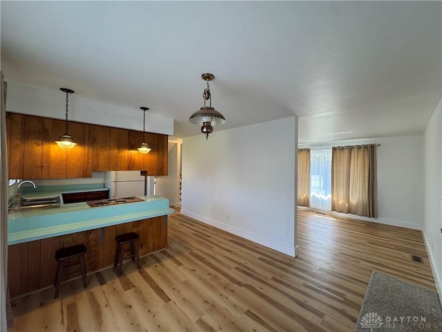 kitchen with a breakfast bar area, a sink, hanging light fixtures, light wood-type flooring, and brown cabinets