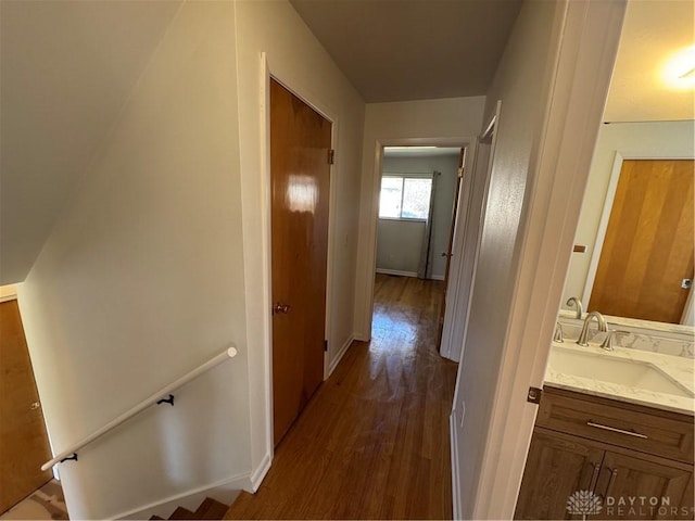 hallway with dark wood-style floors, baseboards, a sink, and an upstairs landing