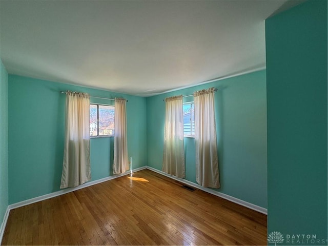 empty room featuring hardwood / wood-style flooring, baseboards, and visible vents