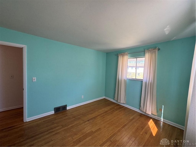 empty room featuring wood finished floors, visible vents, and baseboards