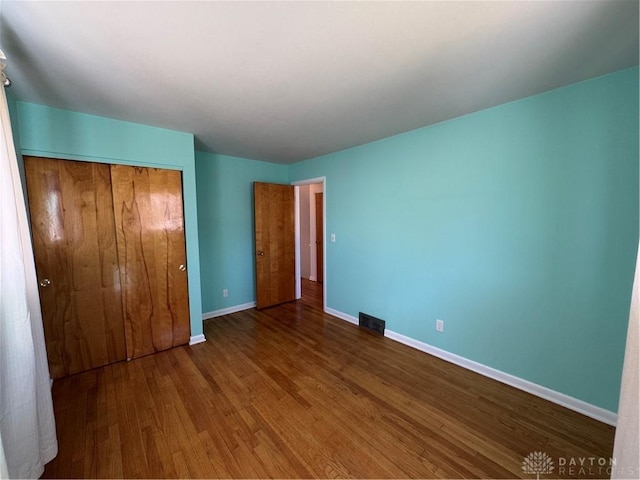 unfurnished bedroom with a closet, visible vents, baseboards, and wood finished floors