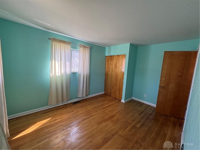 unfurnished bedroom with hardwood / wood-style floors, a closet, visible vents, and baseboards