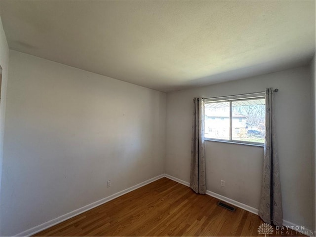 spare room with visible vents, baseboards, and wood finished floors