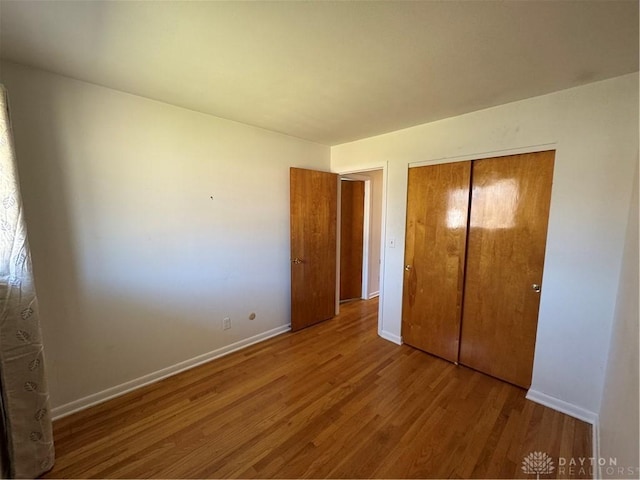 unfurnished bedroom with a closet, wood finished floors, and baseboards