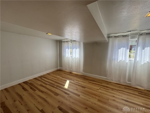 empty room with a textured ceiling, baseboards, and wood finished floors