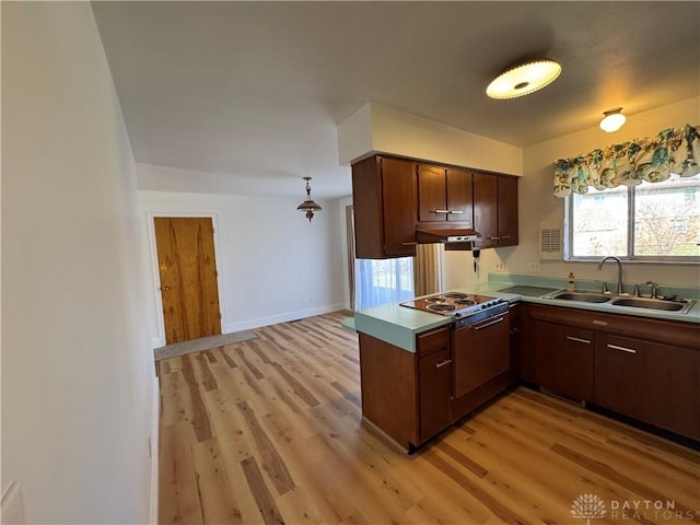 kitchen featuring a peninsula, light wood finished floors, a sink, and baseboards