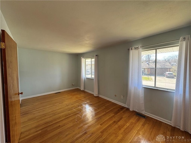 empty room with visible vents, light wood-style flooring, and baseboards