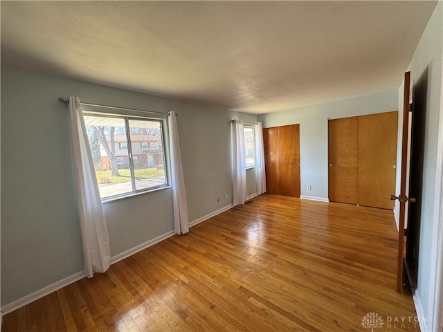 unfurnished bedroom with multiple windows, light wood-style flooring, baseboards, and two closets