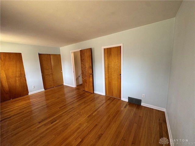 unfurnished bedroom featuring visible vents, two closets, baseboards, and wood finished floors