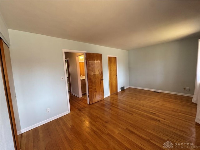 unfurnished bedroom with a closet, wood finished floors, visible vents, and baseboards