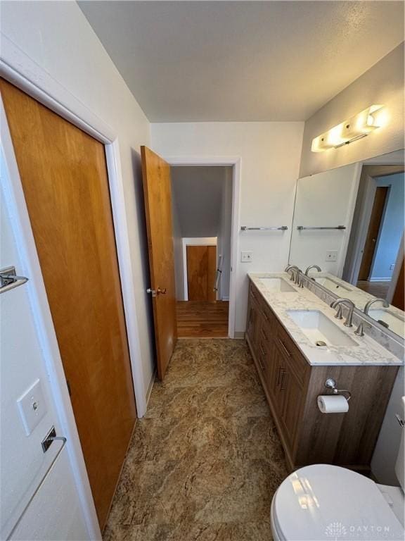 bathroom with toilet, double vanity, and a sink