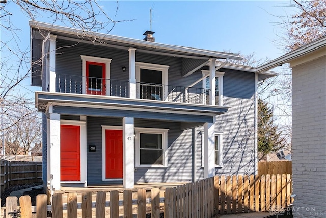 view of front of house with a fenced front yard, a chimney, covered porch, and a balcony