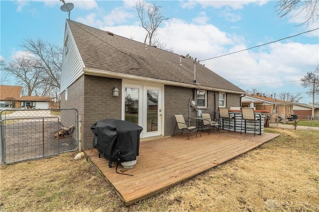 rear view of house featuring roof with shingles, fence, a deck, and brick siding