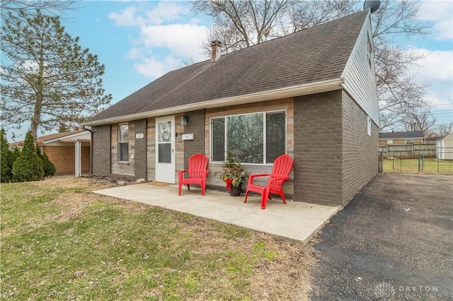 rear view of property with brick siding, roof with shingles, a lawn, a patio area, and fence