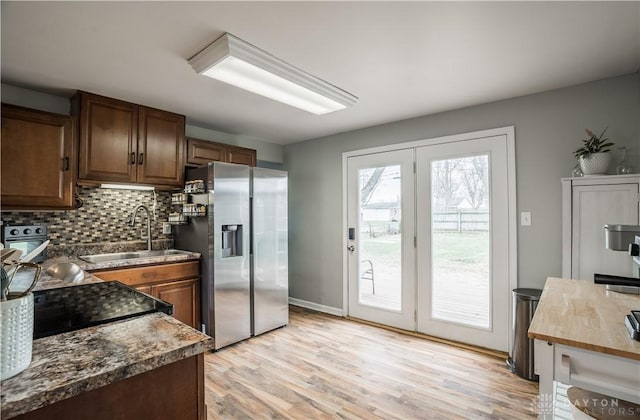 kitchen featuring light wood-style flooring, a sink, backsplash, dark countertops, and stainless steel fridge