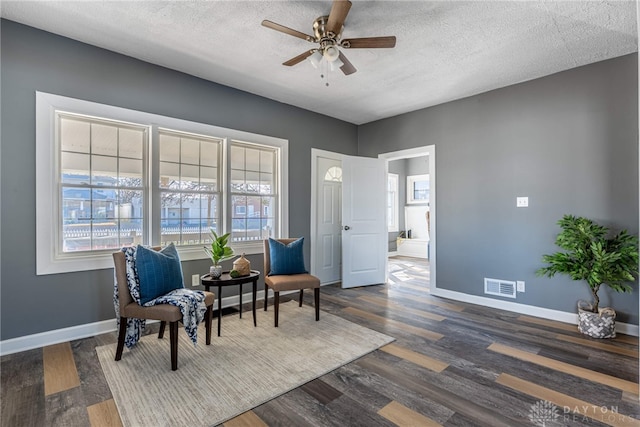 living area featuring baseboards, visible vents, a ceiling fan, dark wood-style floors, and a textured ceiling