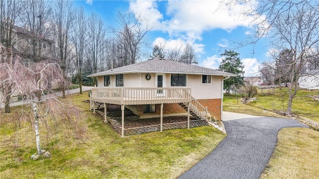 rear view of property featuring a shingled roof, stairway, aphalt driveway, a yard, and a wooden deck