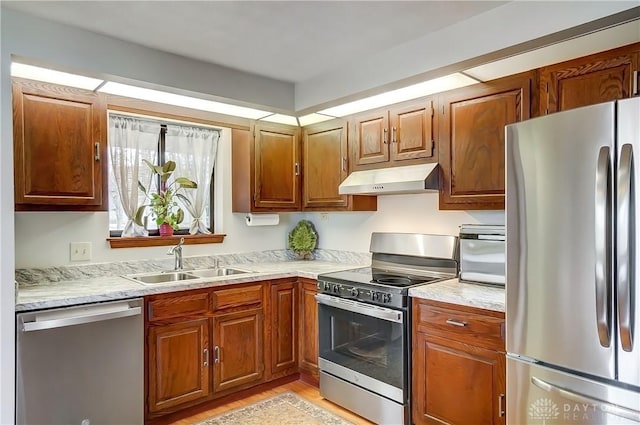 kitchen with brown cabinets, appliances with stainless steel finishes, light wood-style floors, a sink, and under cabinet range hood