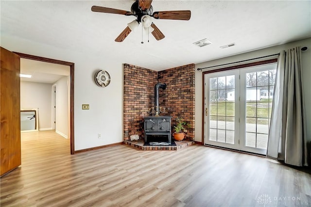 unfurnished living room with ceiling fan, wood finished floors, visible vents, baseboards, and a wood stove